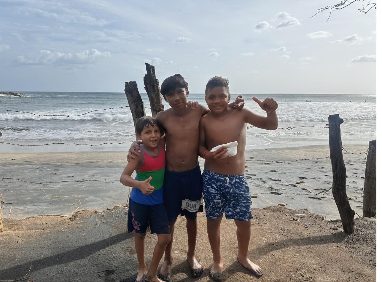 Three young boys standing on the beach in front of the ocean